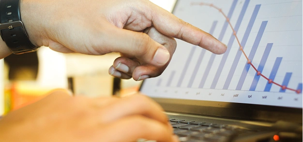 Person pointing at a declining chart on a laptop screen